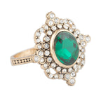 Gold ring with a green gemstone and clear stones on a white background