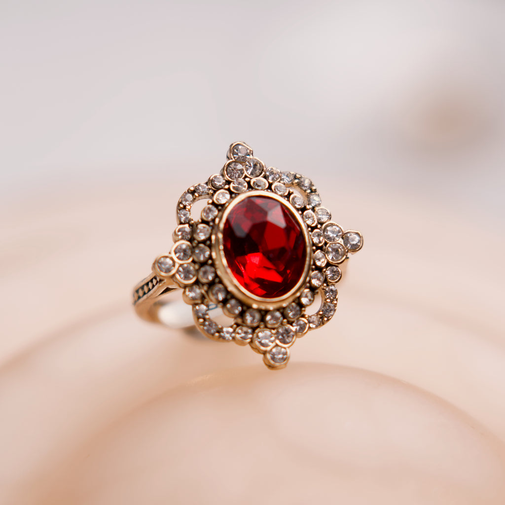 Gold ring with a red gemstone on a soft beige background