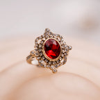 Gold ring with a red gemstone on a soft beige background