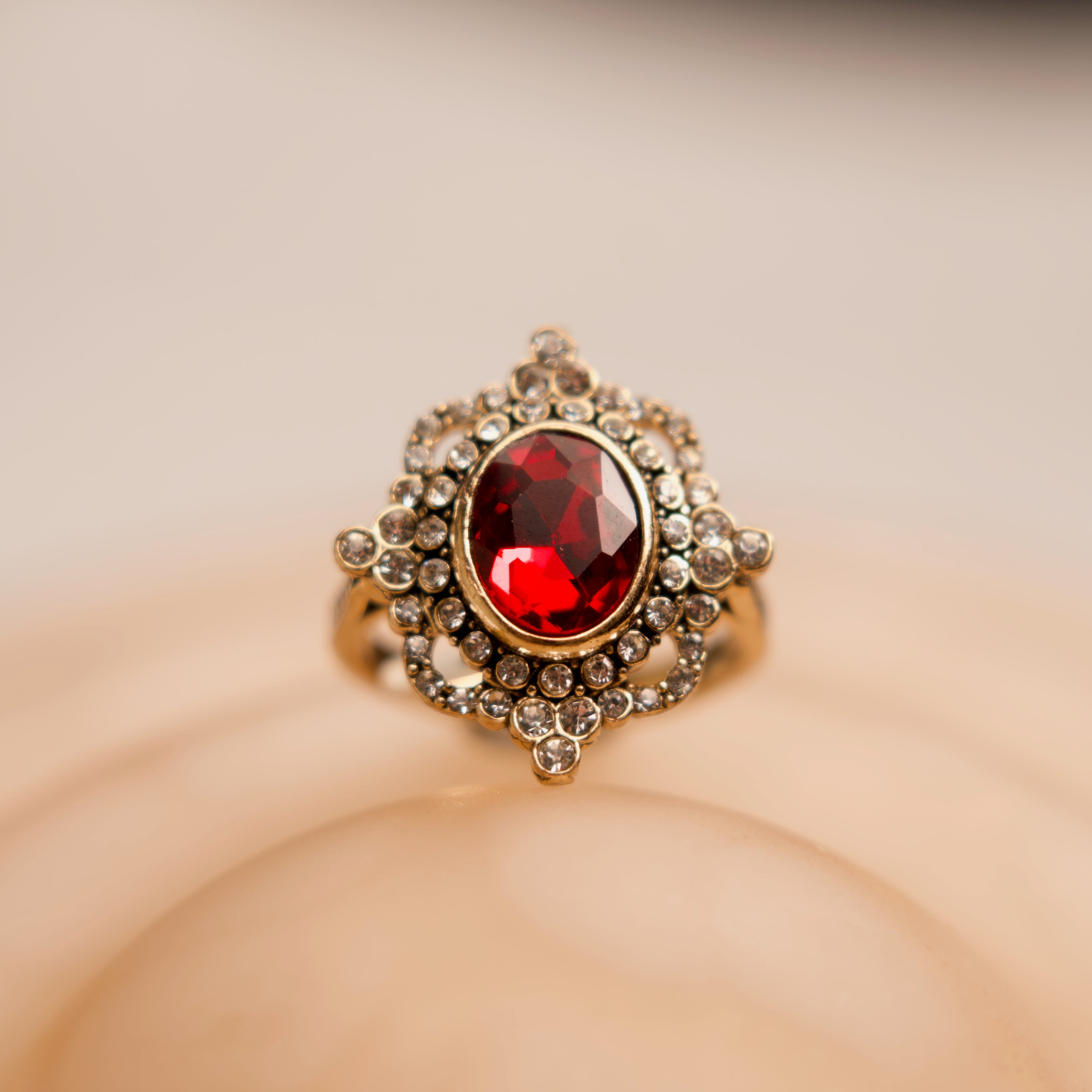 Gold ring with a red gemstone on a beige background