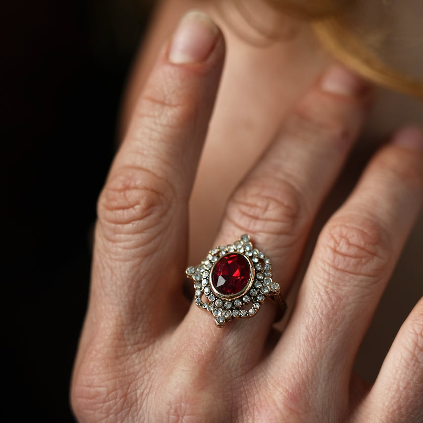Close-up of a hand wearing a decorative ring with a red gemstone on a blurred background