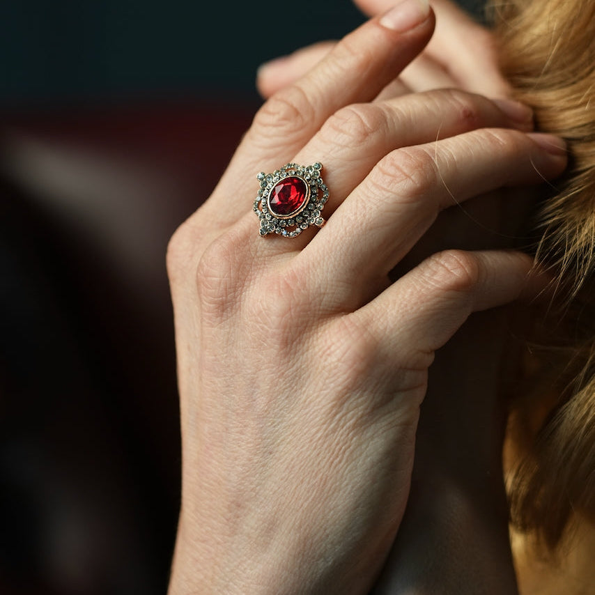 Close-up of a hand wearing a ring with a red gemstone against a dark background