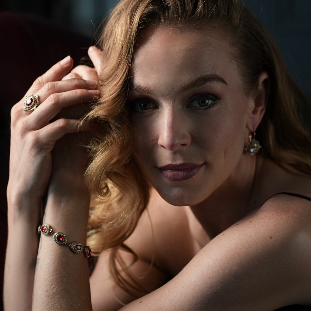 Woman with red hair and makeup posing with hand by face against a dark background