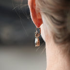 Close-up of a person wearing a gold earring with a small pendant.