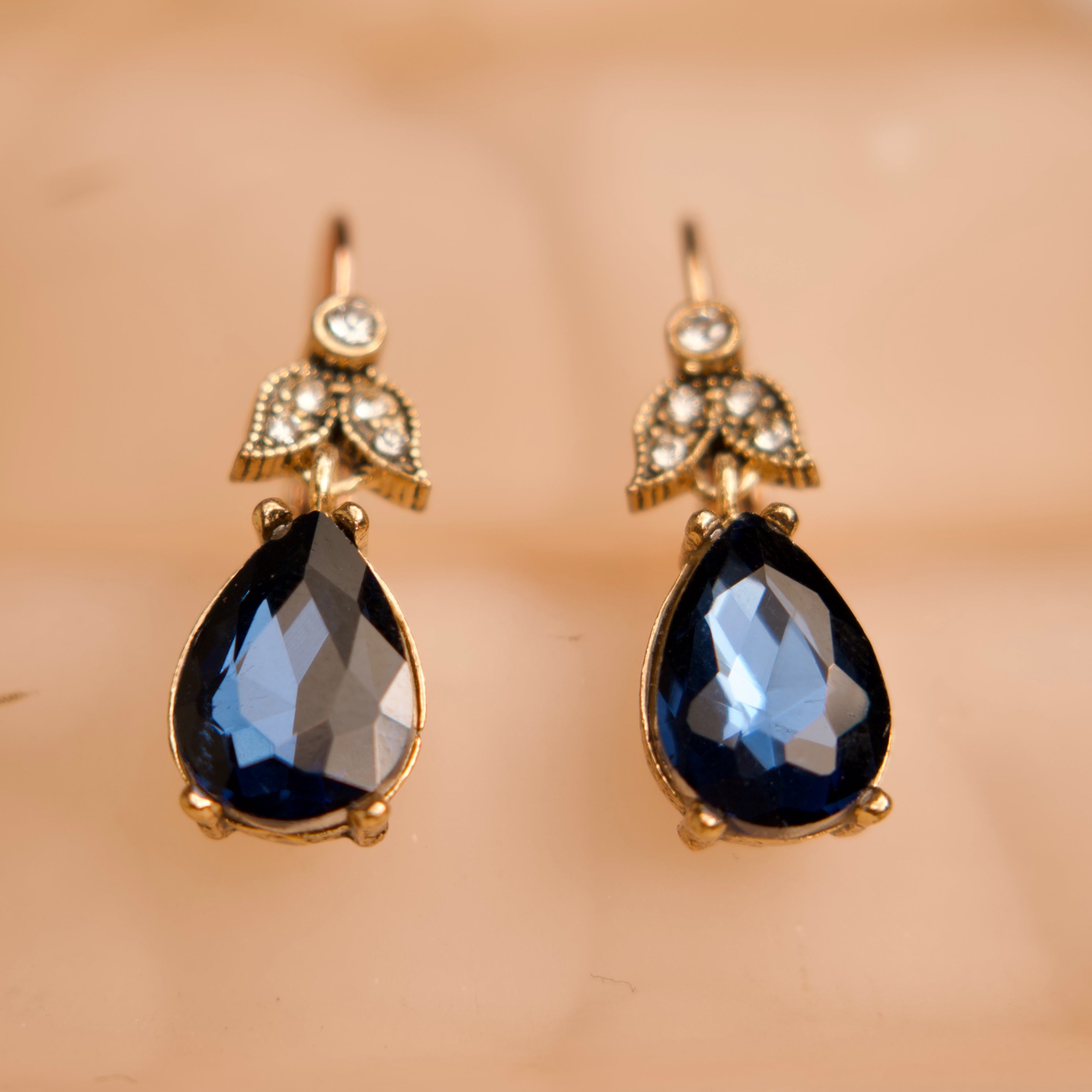 Pair of gold earrings with blue teardrop stones on a beige background