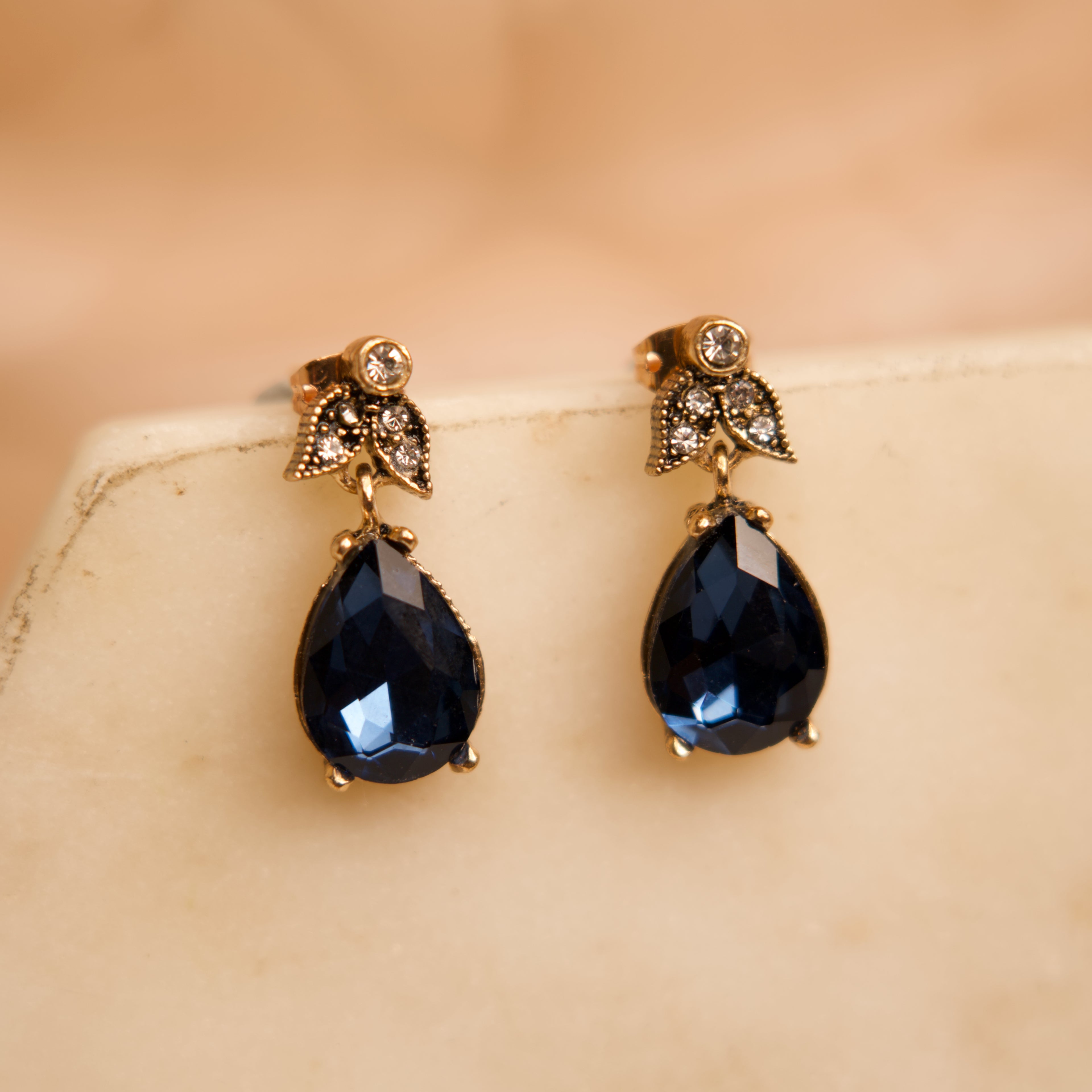 Pair of black teardrop earrings with gold accents on a beige surface.