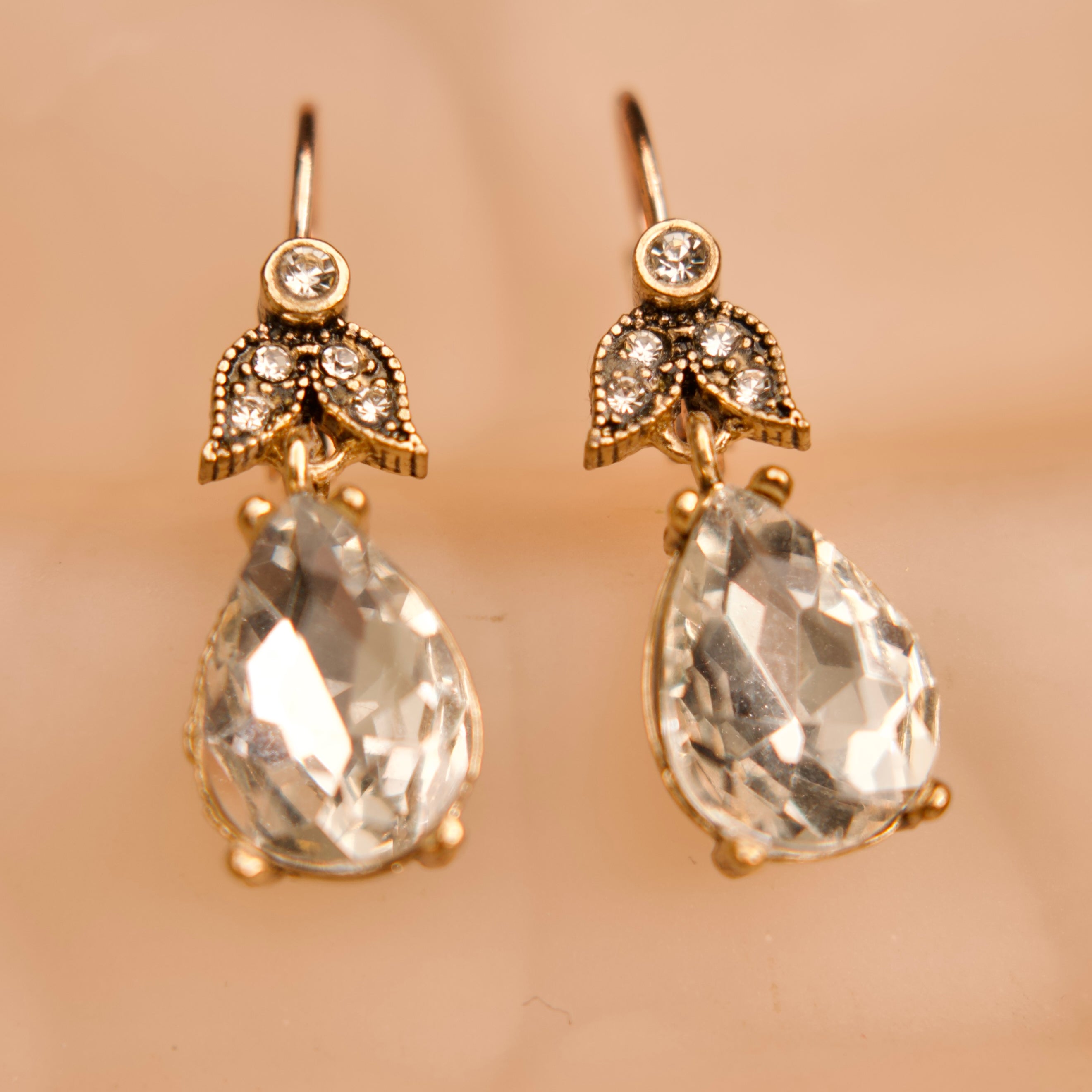 Pair of gold earrings with teardrop-shaped crystals on a beige background
