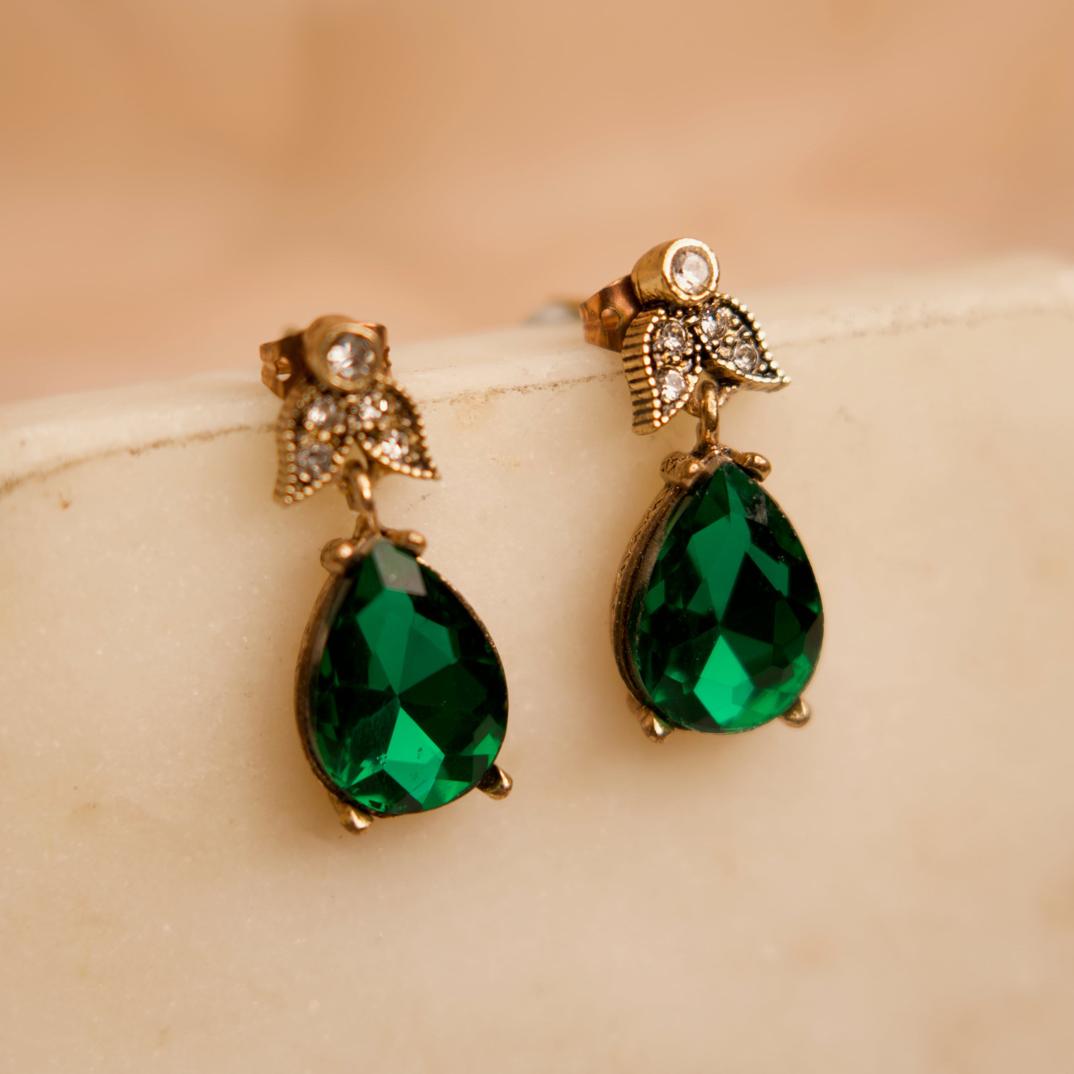 Pair of green teardrop earrings with gold accents on a beige surface