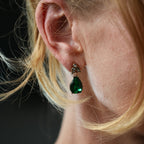 Close-up of a person wearing a green teardrop earring with a blurred background