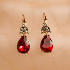 Pair of red teardrop earrings with gold and gemstone accents on a beige background