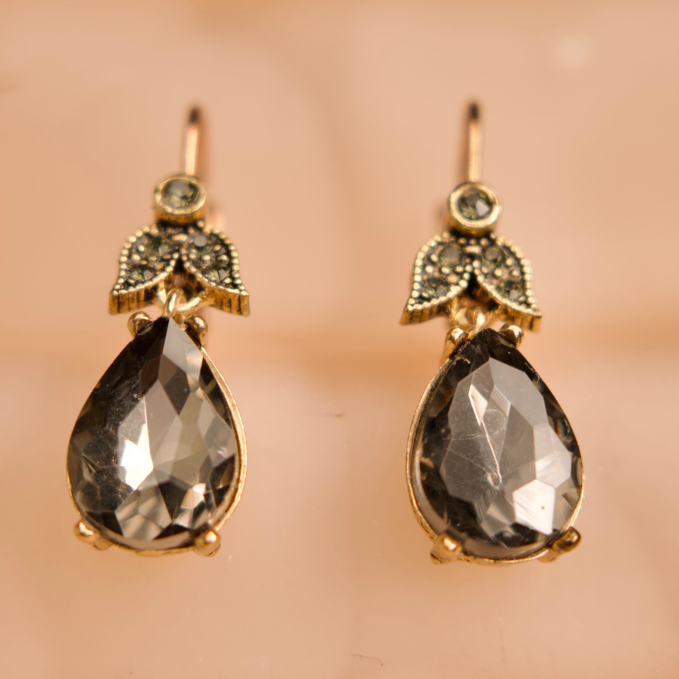 Pair of gold earrings with teardrop-shaped gemstones on a beige background