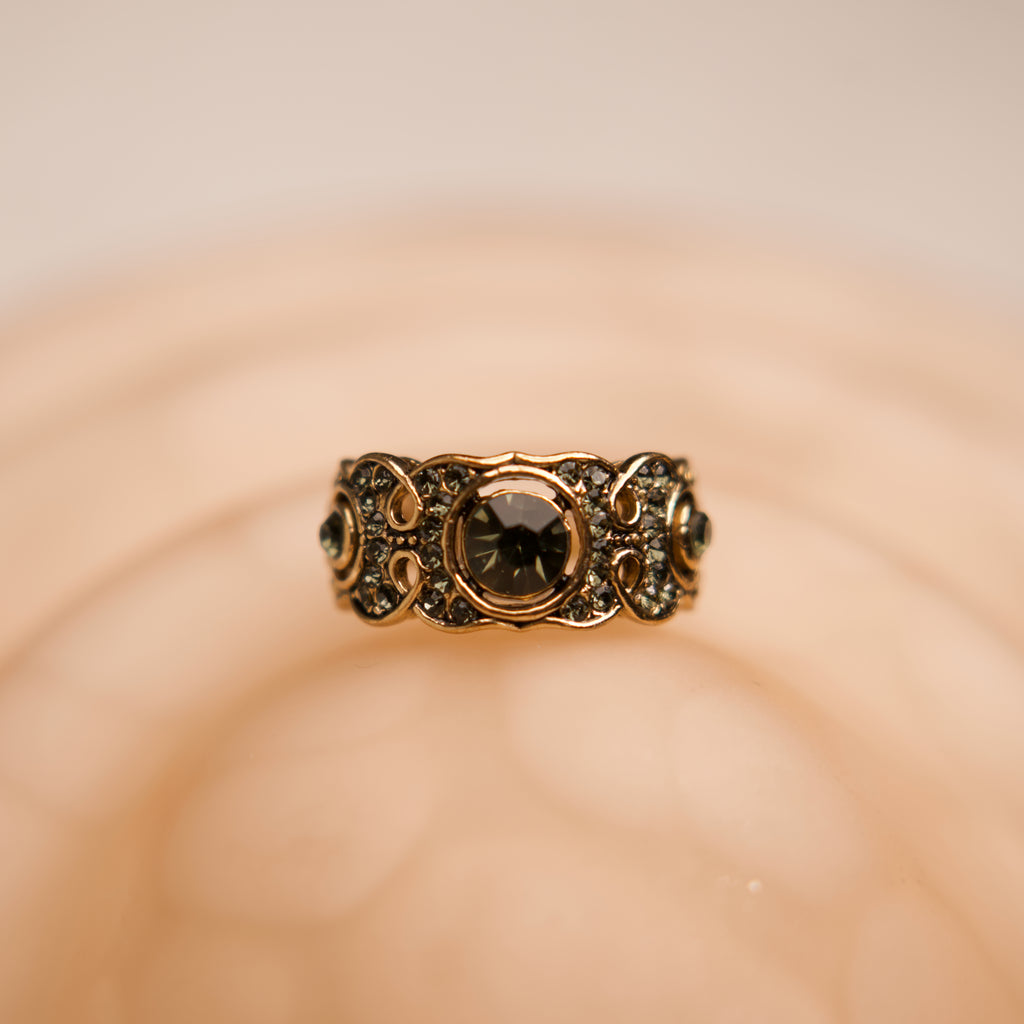 Gold ring with a central black gemstone on a blurred beige background