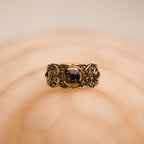 Gold ring with a central black gemstone on a beige background