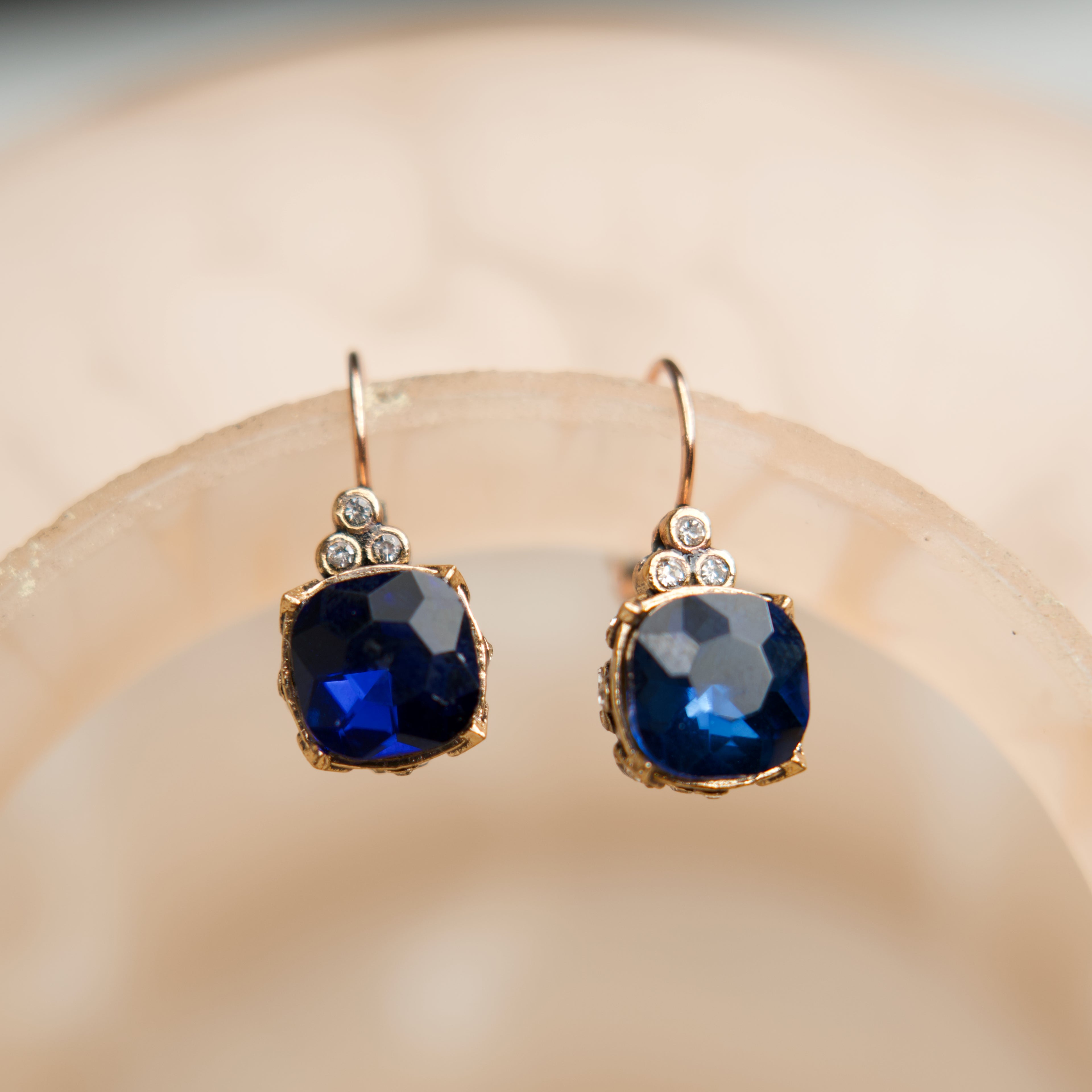 Pair of gold earrings with blue gemstones on a beige background