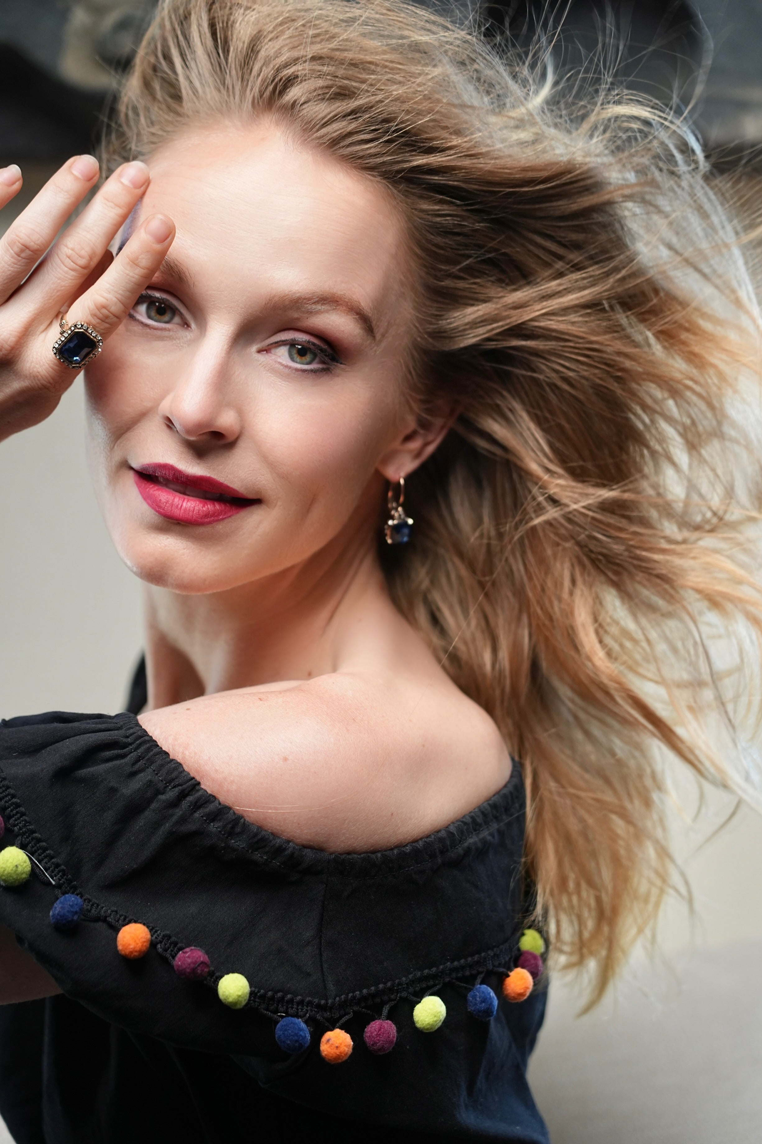 Woman with styled hair and colorful pom-pom details on a dark top