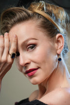 Close-up of a woman with a hand on her face, wearing a ring and earrings.