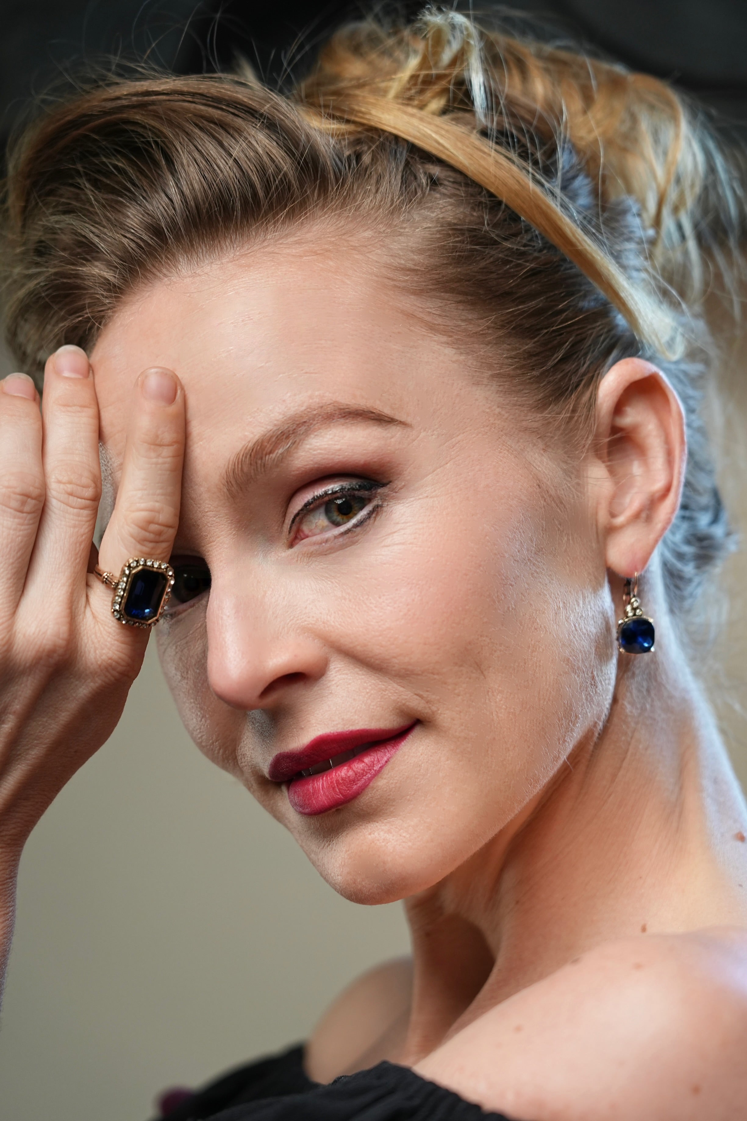Close-up of a woman with a hand on her face, wearing a ring and earrings.