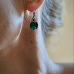 Close-up of an ear wearing a green gemstone earring with a blurred background