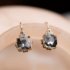 Pair of earrings with dark gemstones on a soft pink background