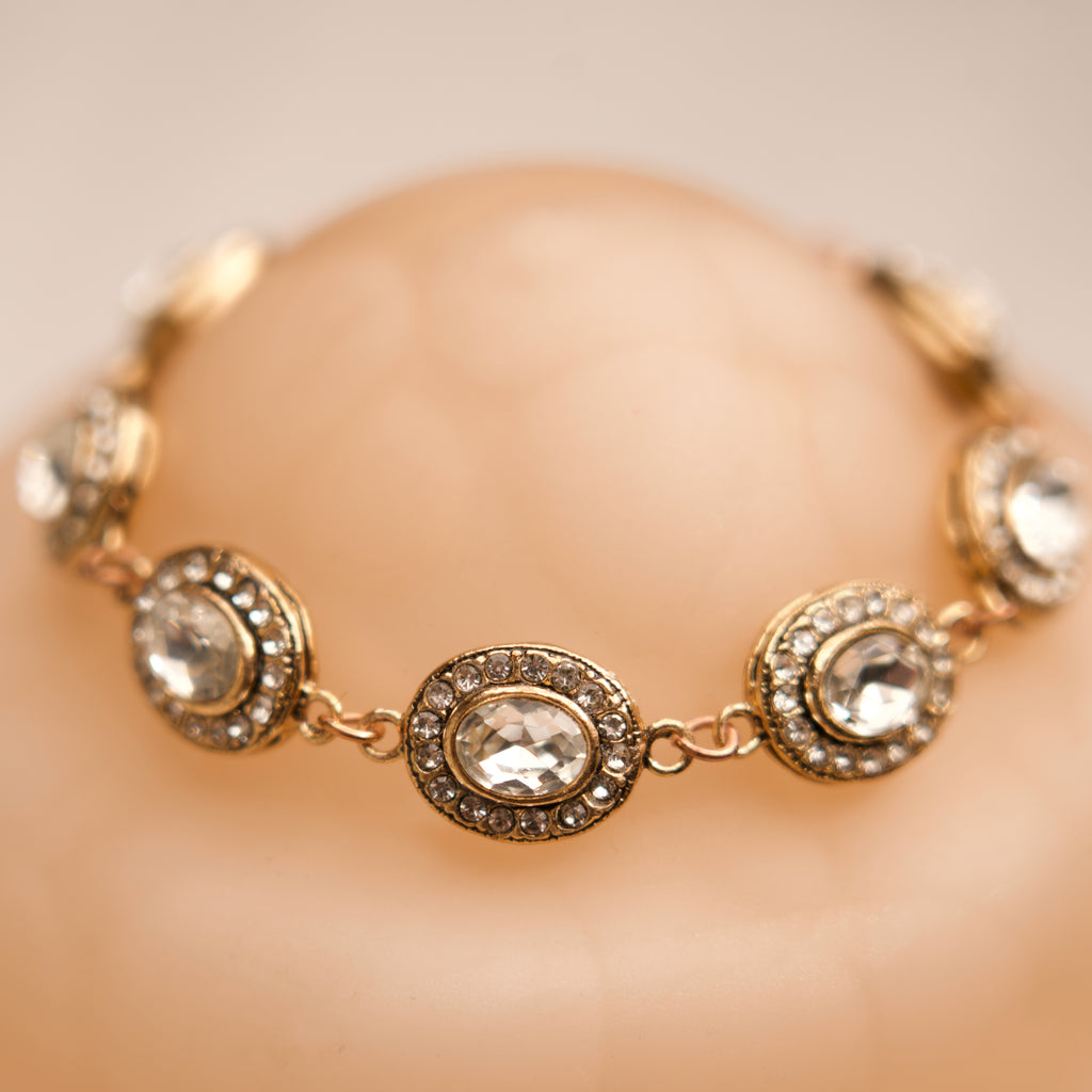 Gold bracelet with clear gemstones on a mannequin hand against a beige background