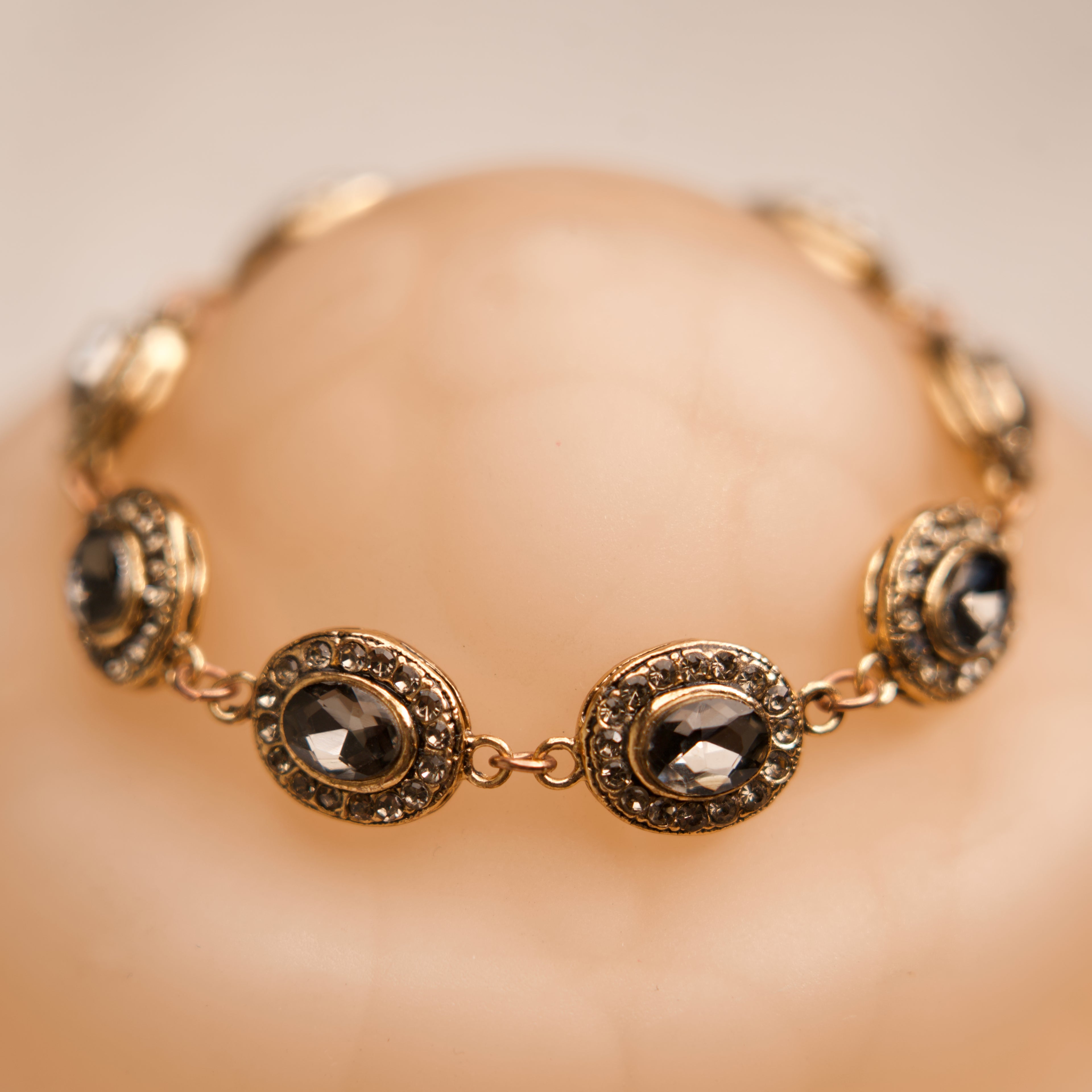 Gold bracelet with gemstones on a mannequin hand against a beige background